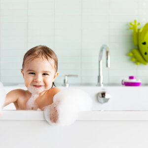 Lifestyle photography of child hanging over bath tub with toys in the background.