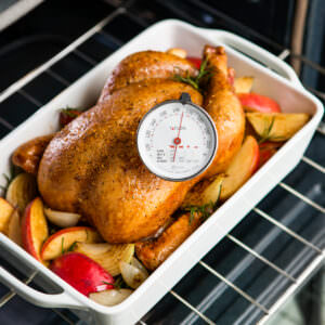 Taylor brand meat thermometer shown in use on a cooking chicken in the oven.