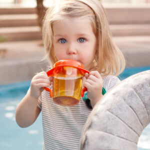 Toddler girl using orange sippy cup outdoors.