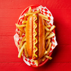 Classic hot dog with fries food photography styled on a vibrant red background.