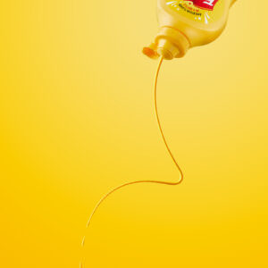 Food photography of mustard being squirted from the bottle in a yellow monochromatic set.